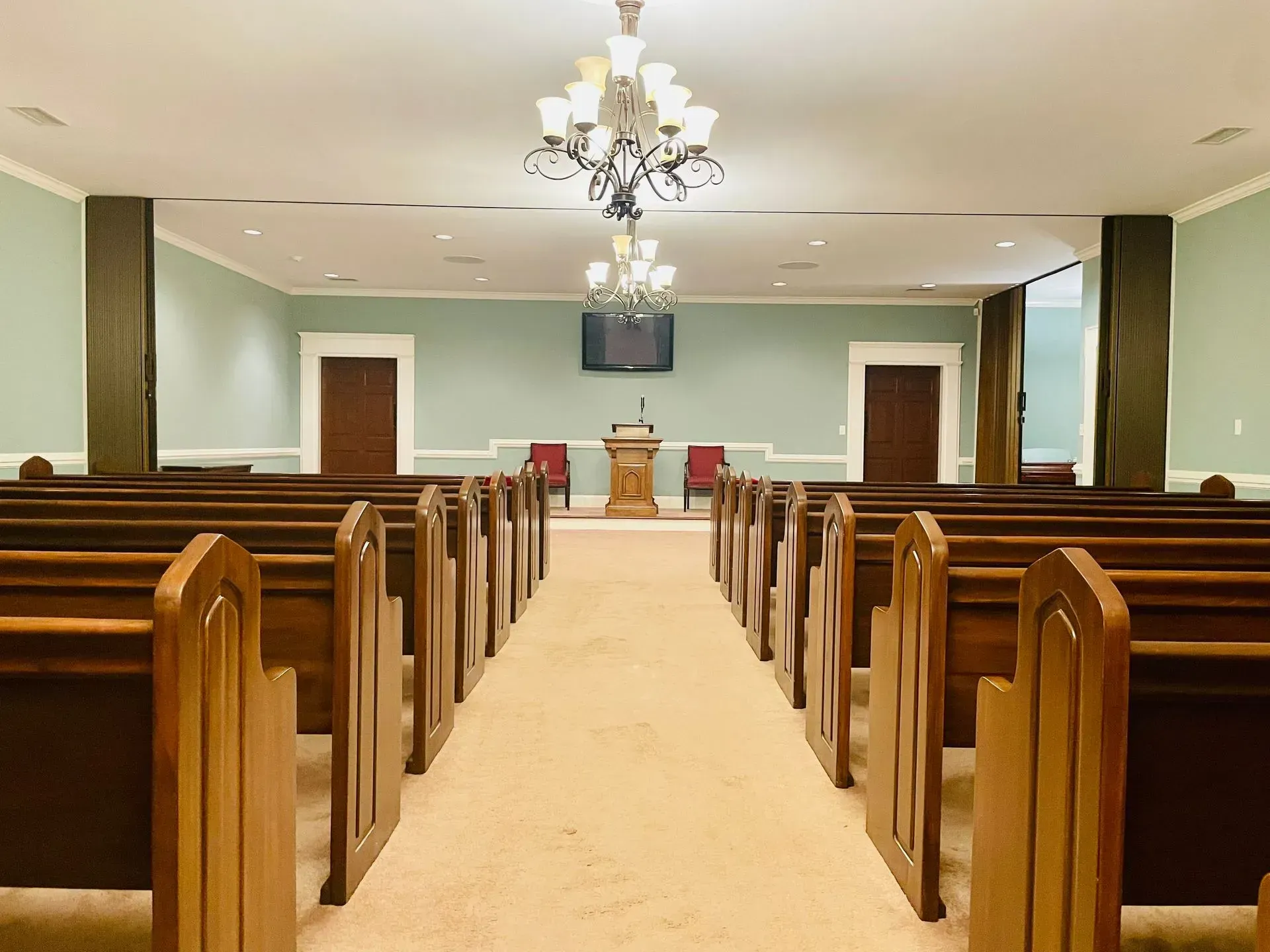 Empty church sanctuary with wooden pews, a center aisle, pulpit, and chandelier under a vaulted ceiling