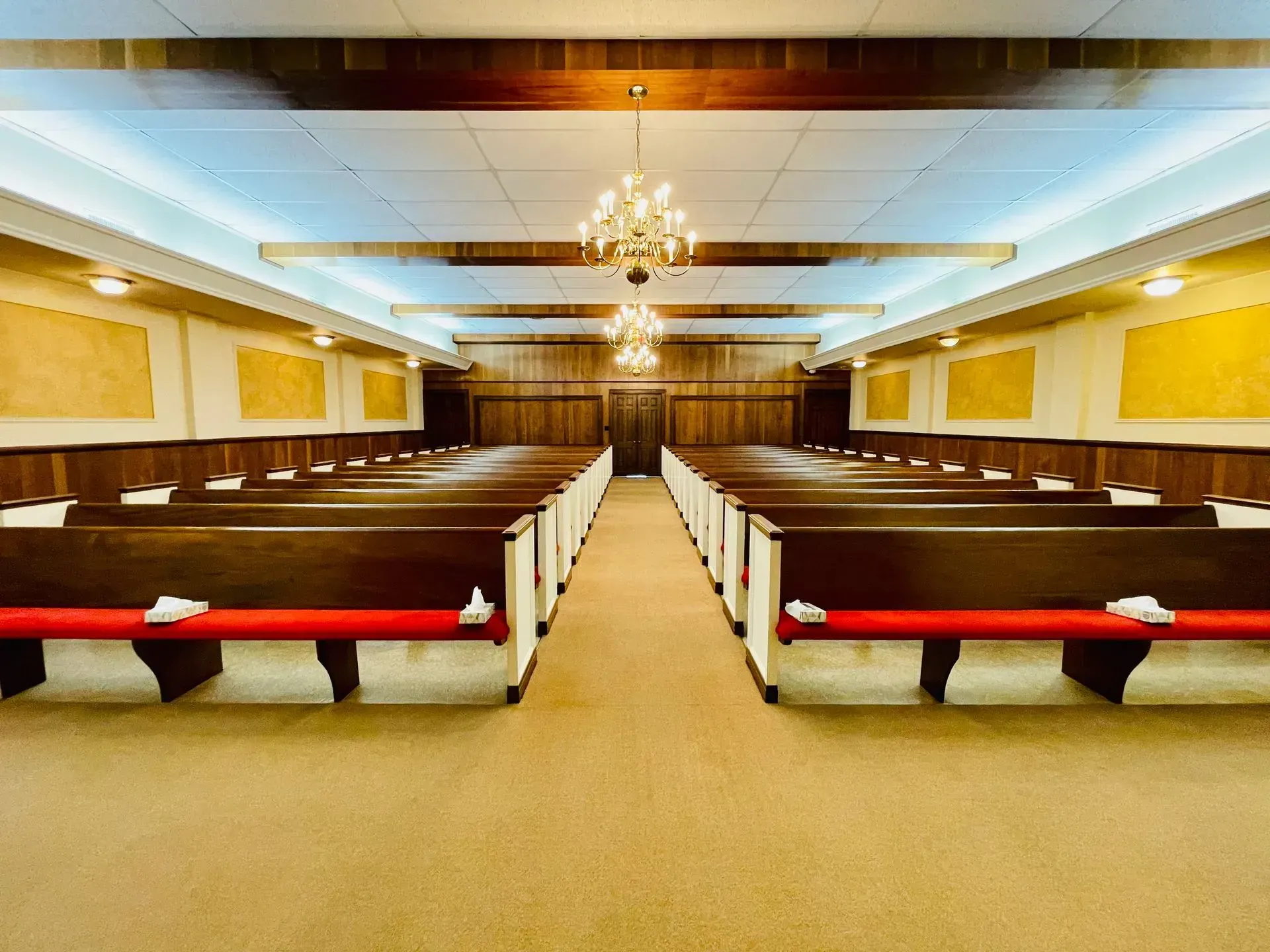 Empty church sanctuary with wooden pews, yellow walls, and a chandelier centered in the aisle