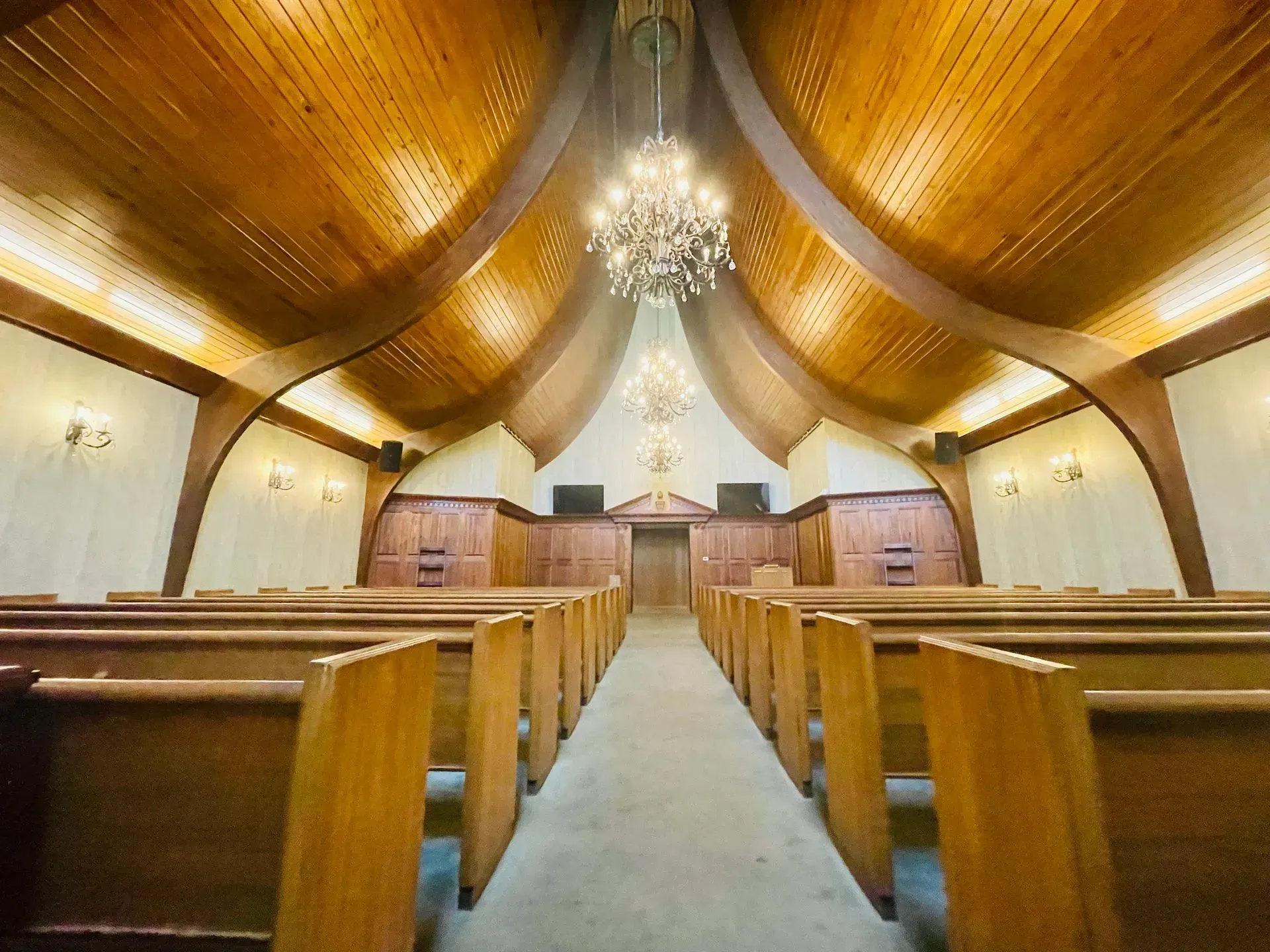 Empty church interior with wooden pews, curved wood ceiling, and central chandelier along the aisle