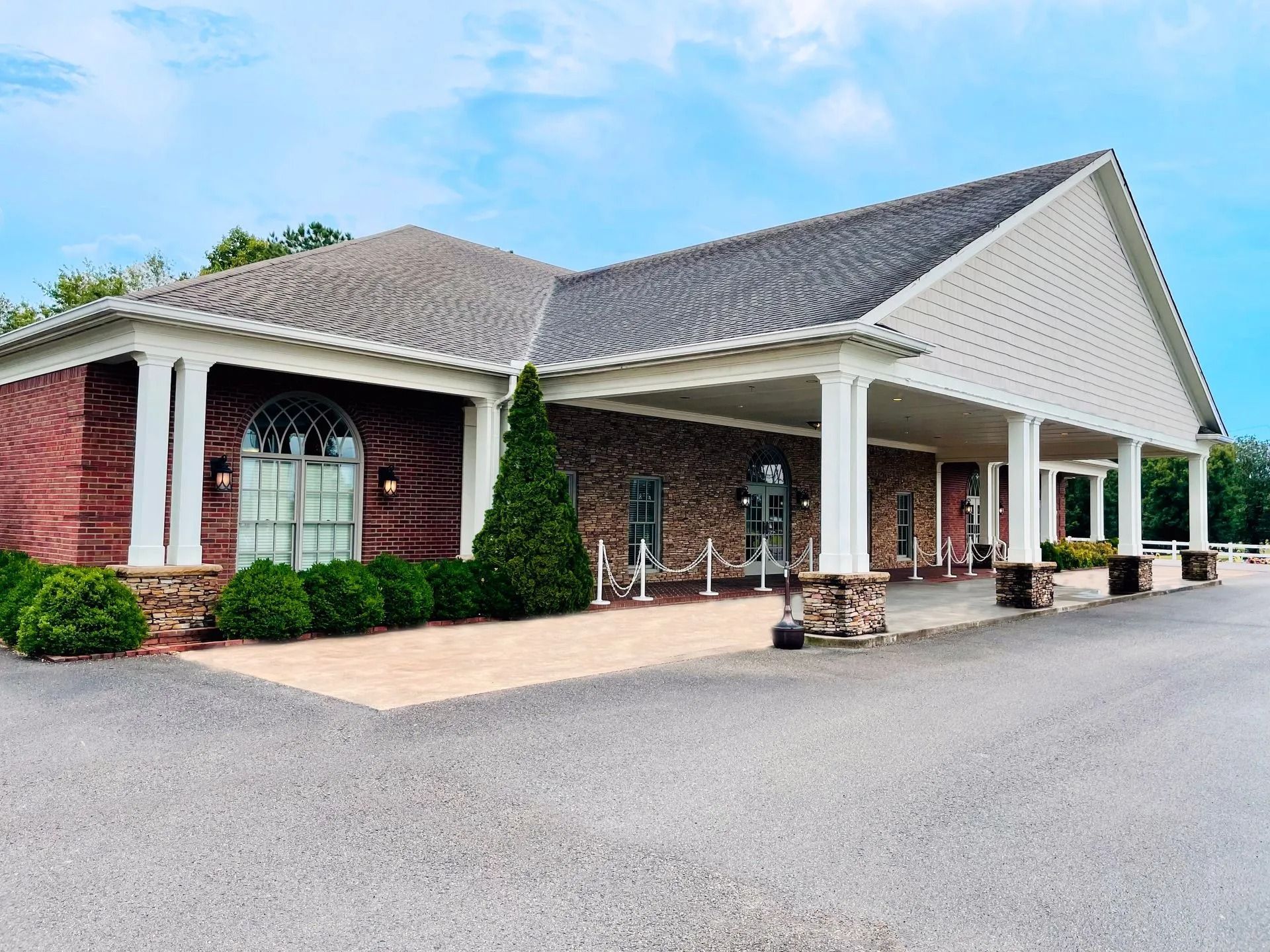 Brick-and-white building with covered entrance and white columns beside a wide paved driveway