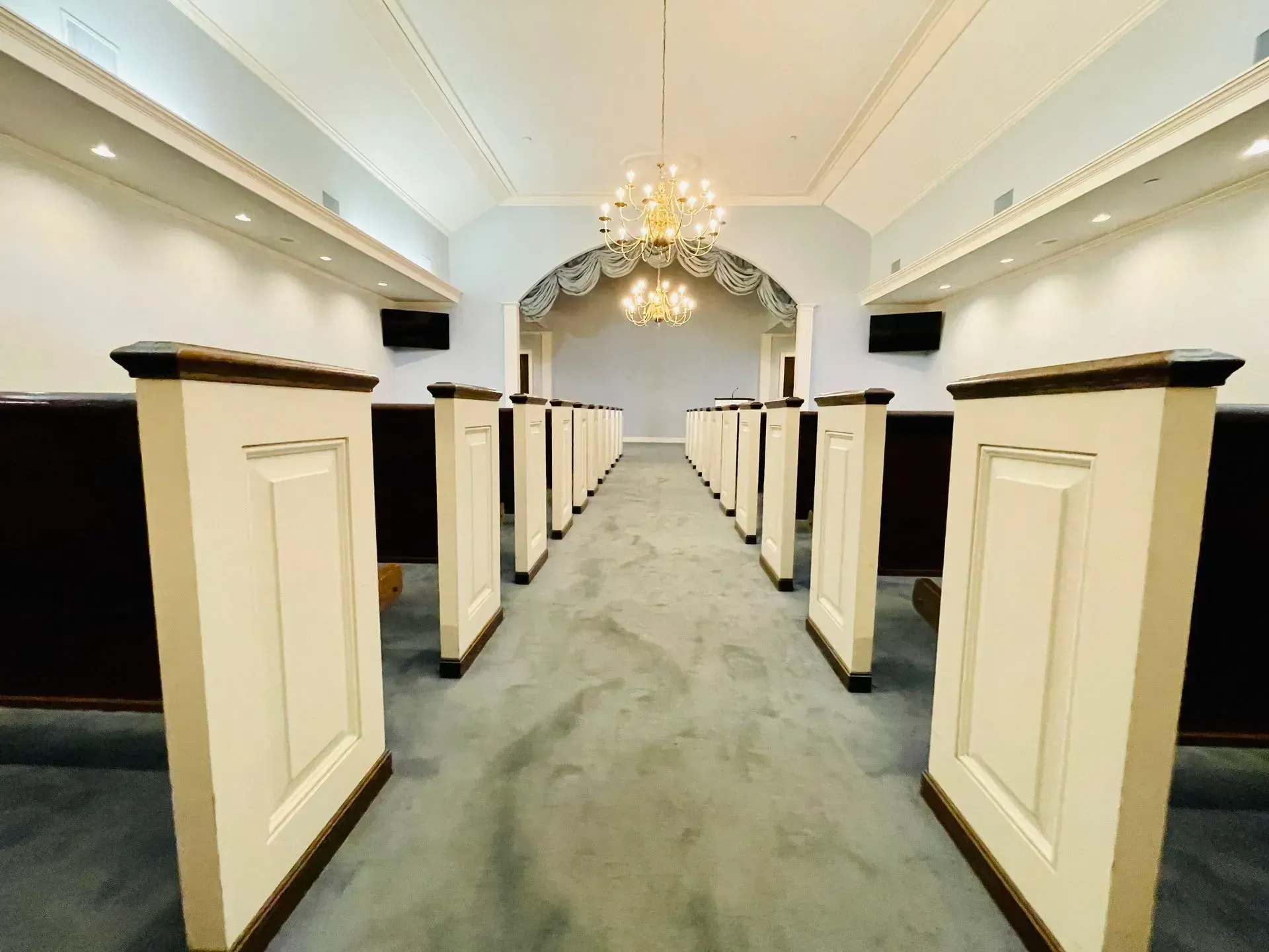 Elegant chapel aisle with white pews, cream walls, and chandelier under an arched ceiling