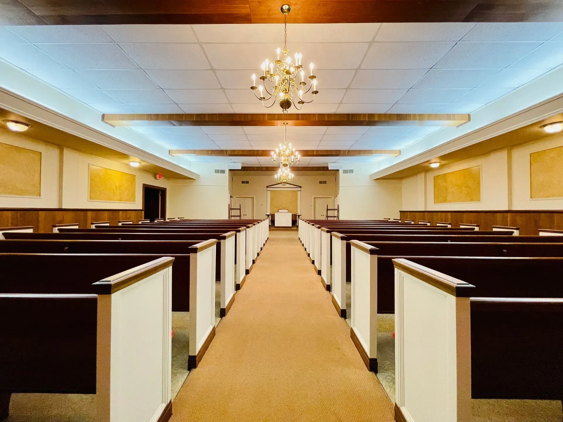 Empty courtroom with rows of wooden benches and a central aisle under chandeliers