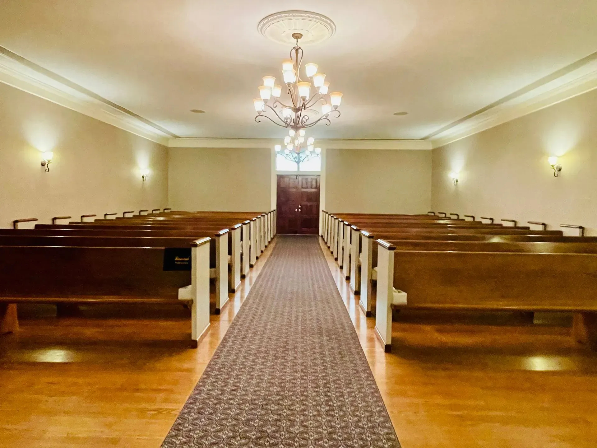 Empty church sanctuary with wooden pews, central aisle, and chandelier lighting