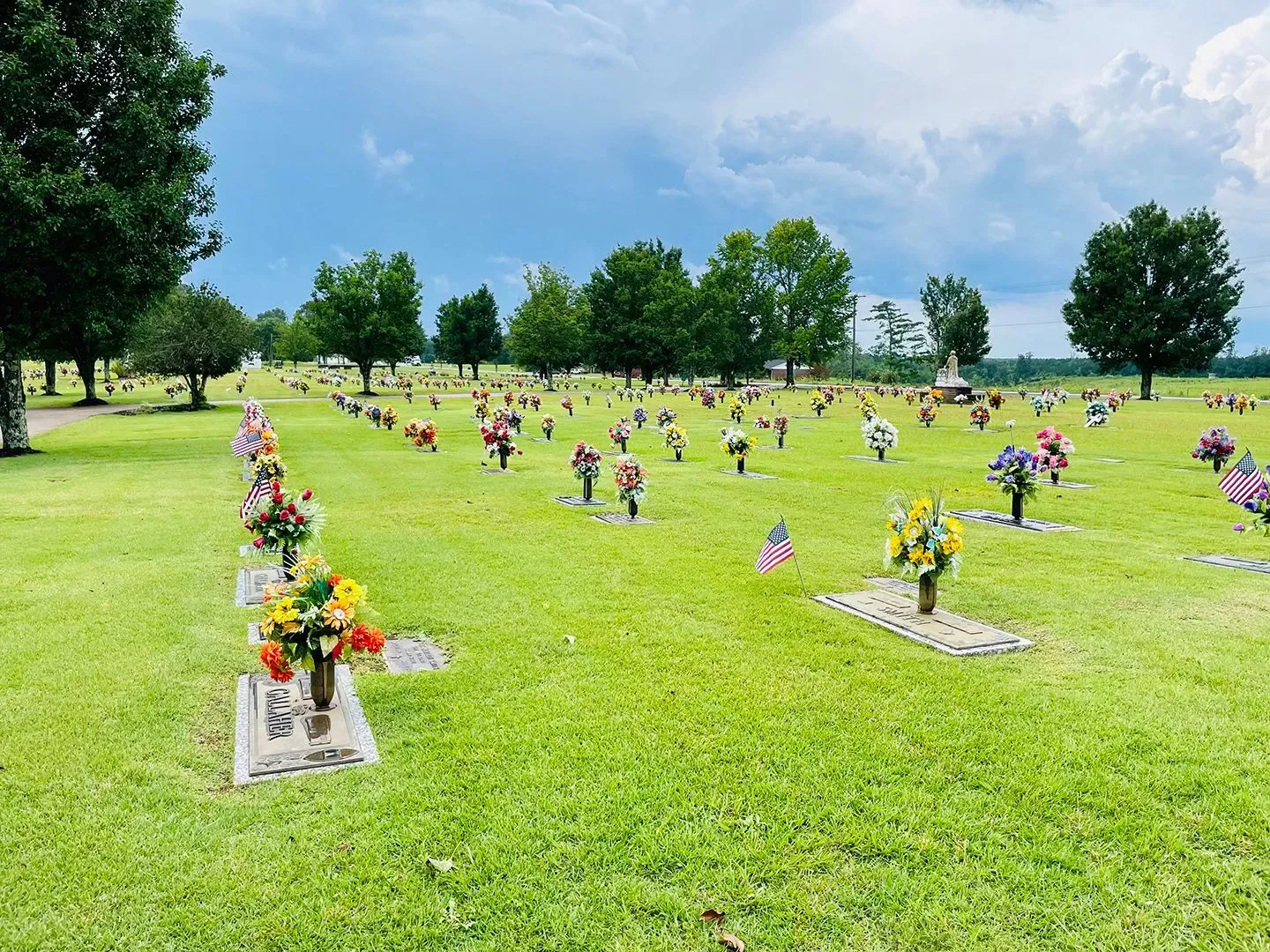 Grassy cemetery with rows of flower-adorned grave markers under a bright sky