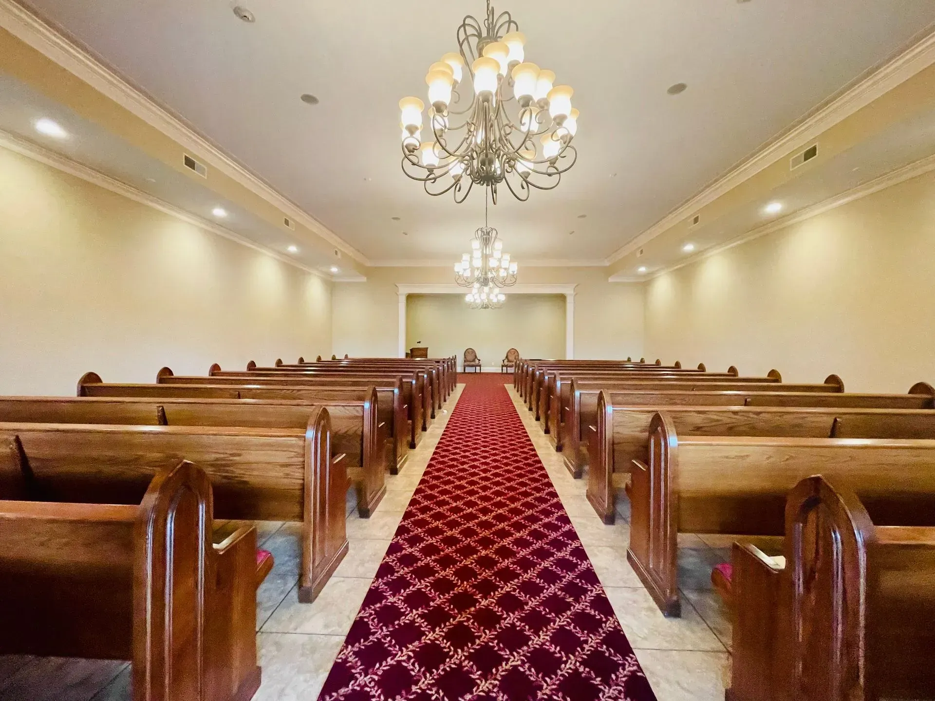 Empty church sanctuary with wooden pews, red carpet aisle, and chandeliers hanging from the ceiling