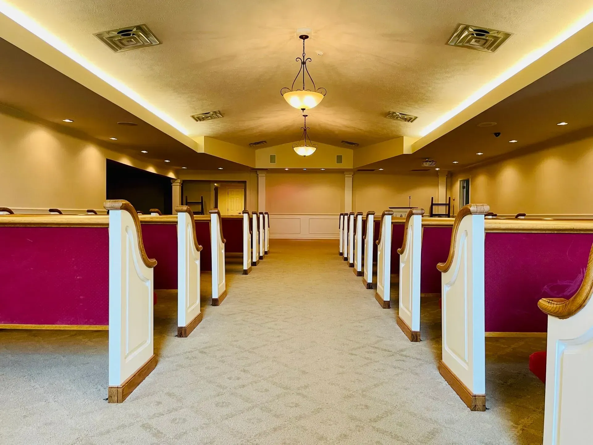 Empty church pews in a beige sanctuary with red cushions and a central aisle