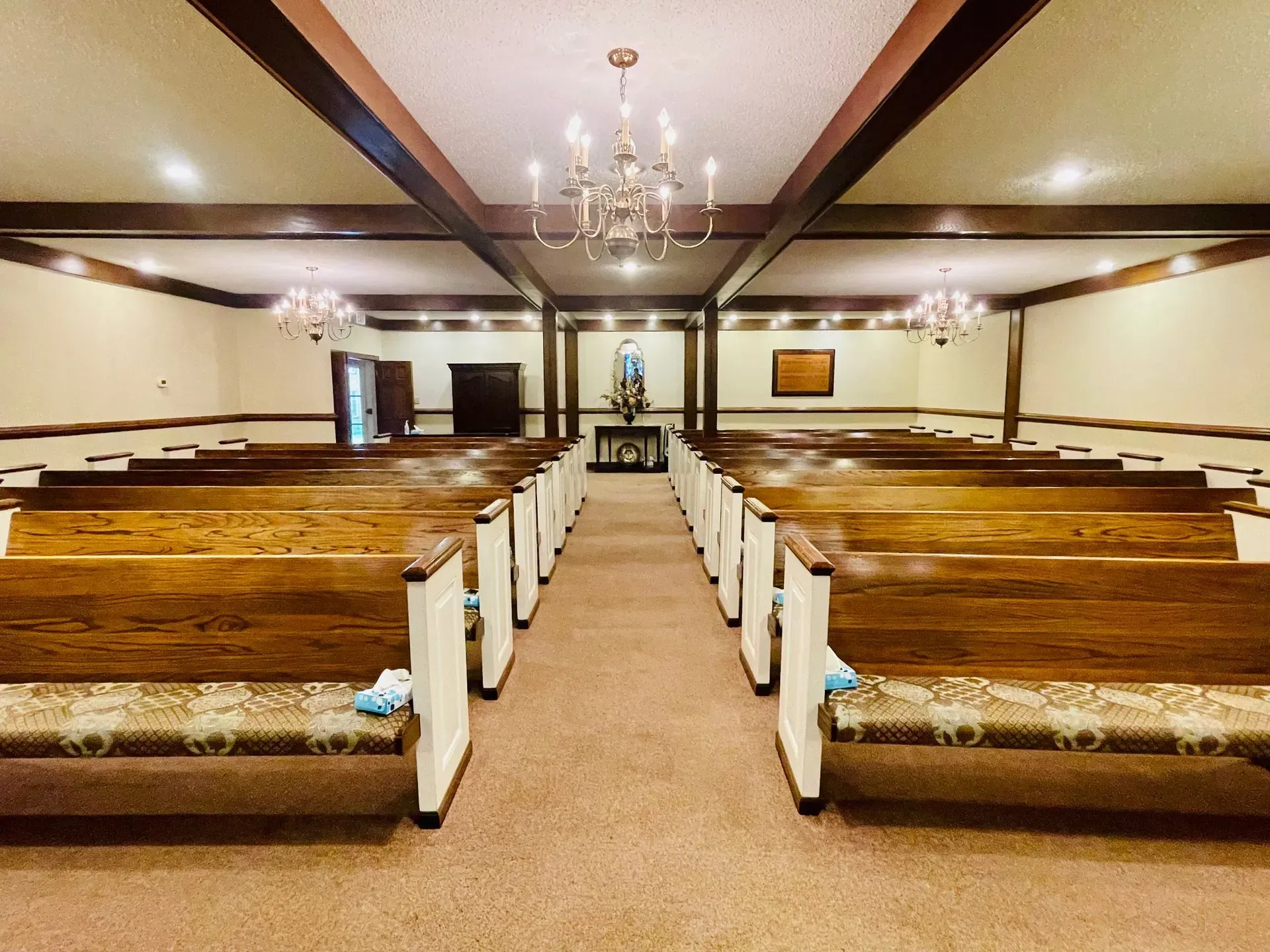 Empty church interior with wooden pews, chandelier, and altar centered at the far end