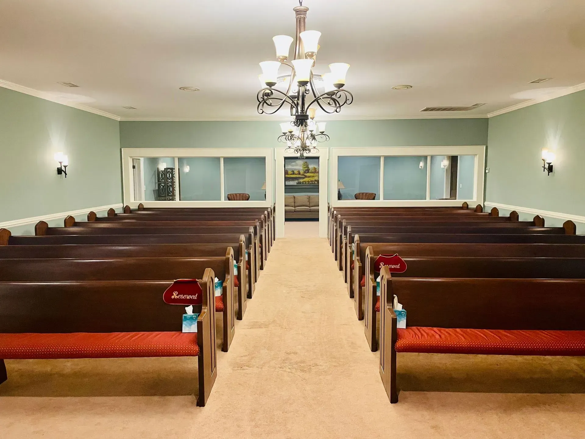 Symmetrical church interior with wooden pews, green walls, chandelier, and red flowers near the aisle.