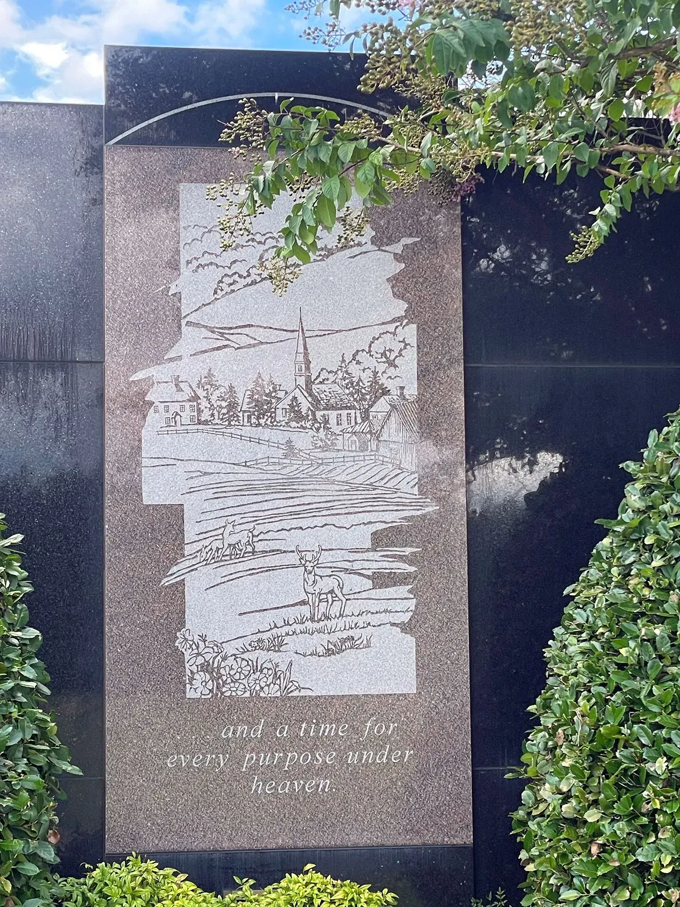 Stone memorial plaque with engraved relief, framed by dark stone and greenery overhead
