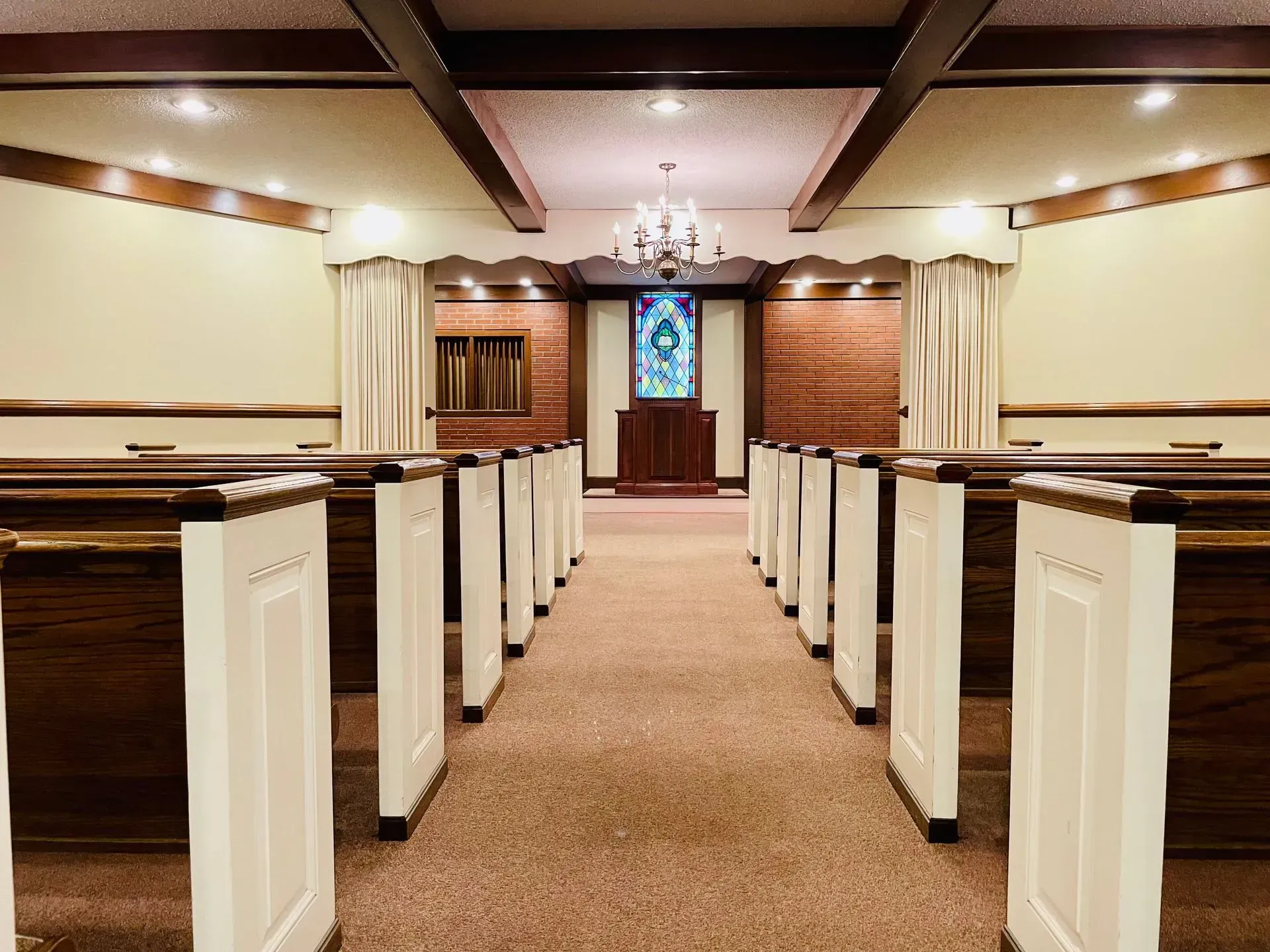 Church sanctuary with wooden pews, carpeted center aisle, and stained-glass window at the front.