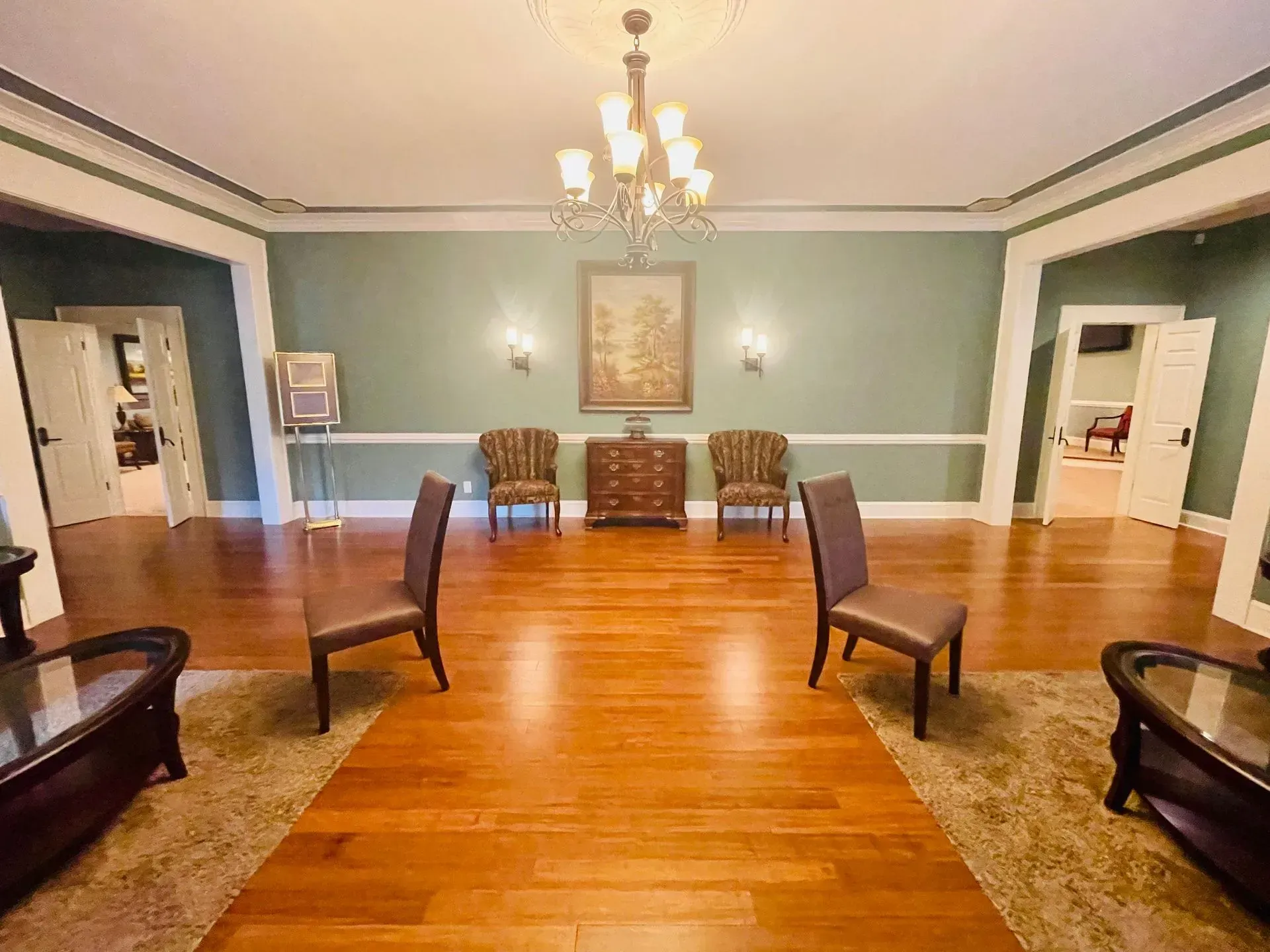 Elegant empty room with green walls, chandelier, wooden floor, and chairs arranged facing the center