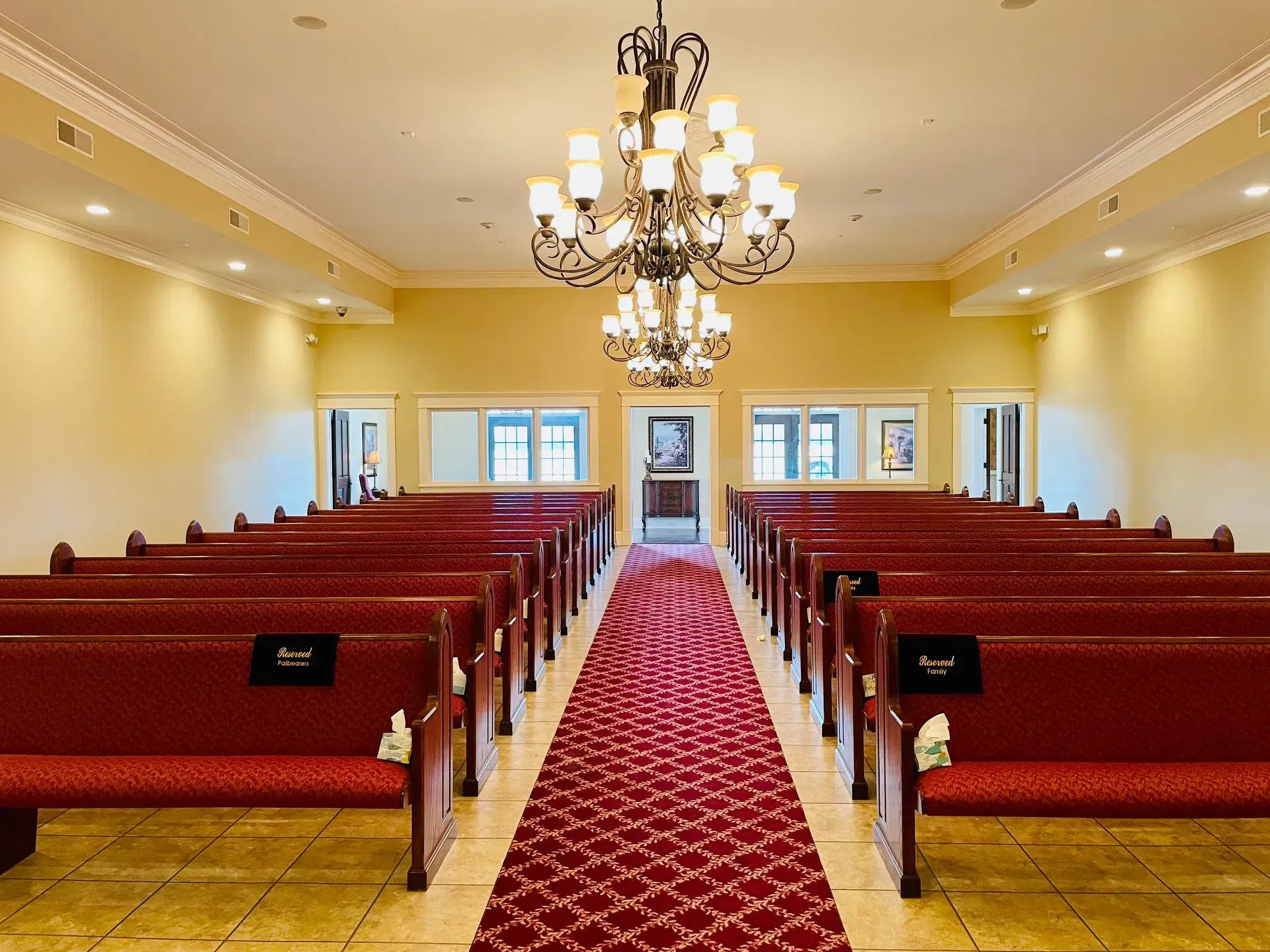 Empty church sanctuary with red pews, gold walls, chandeliers, and a central red carpet aisle