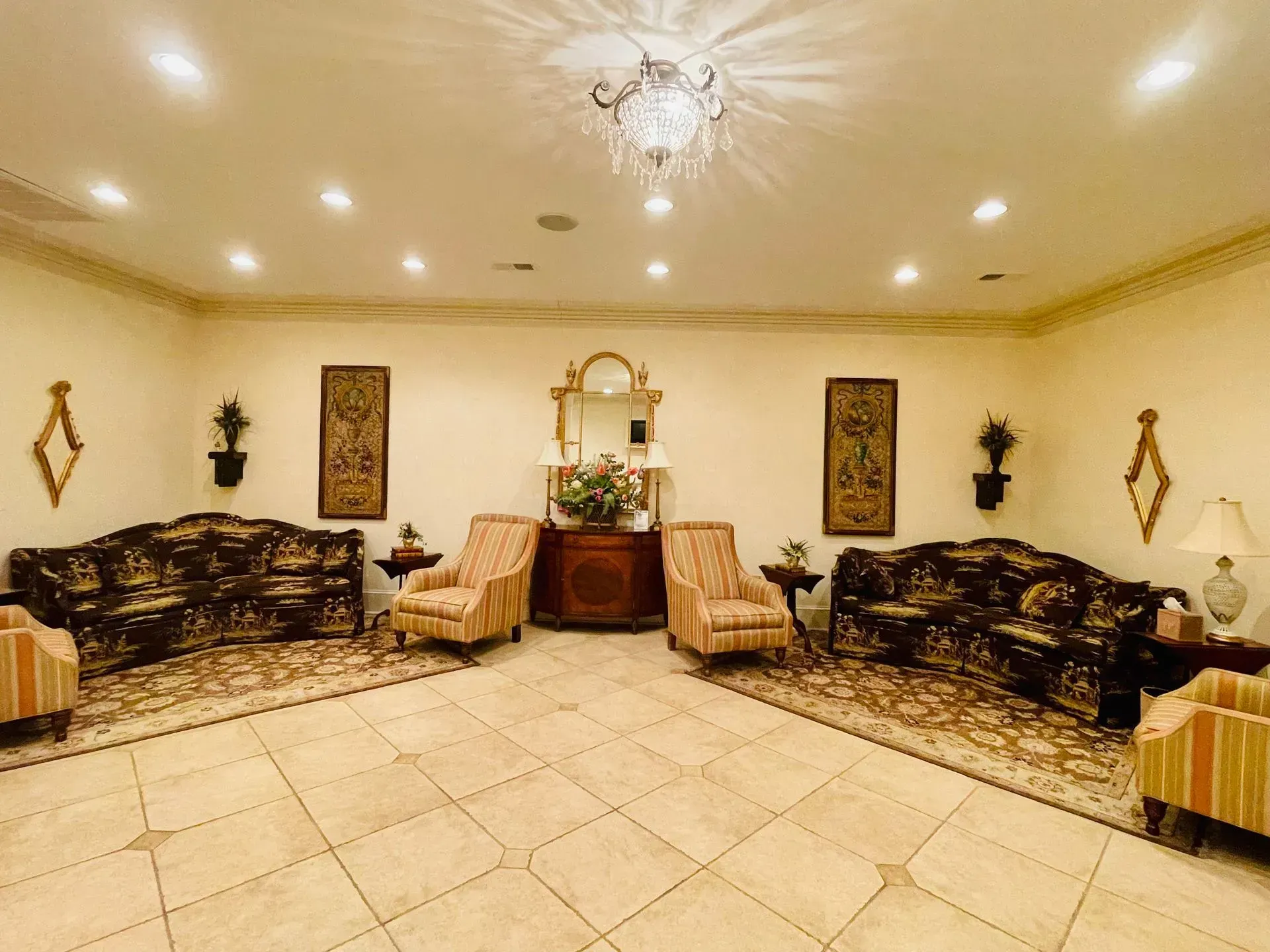 Elegant living room with beige tiled floor, matching dark sofas, wall art, and a chandelier.