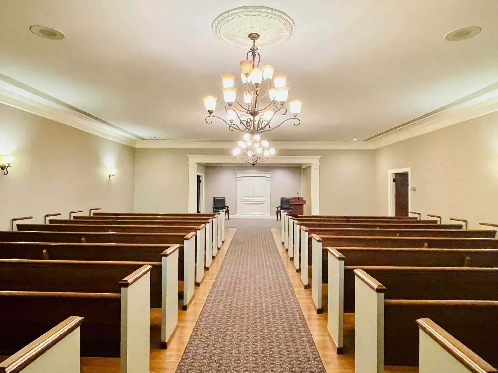 Empty church sanctuary with wooden pews, central aisle, and chandeliers hanging from the ceiling