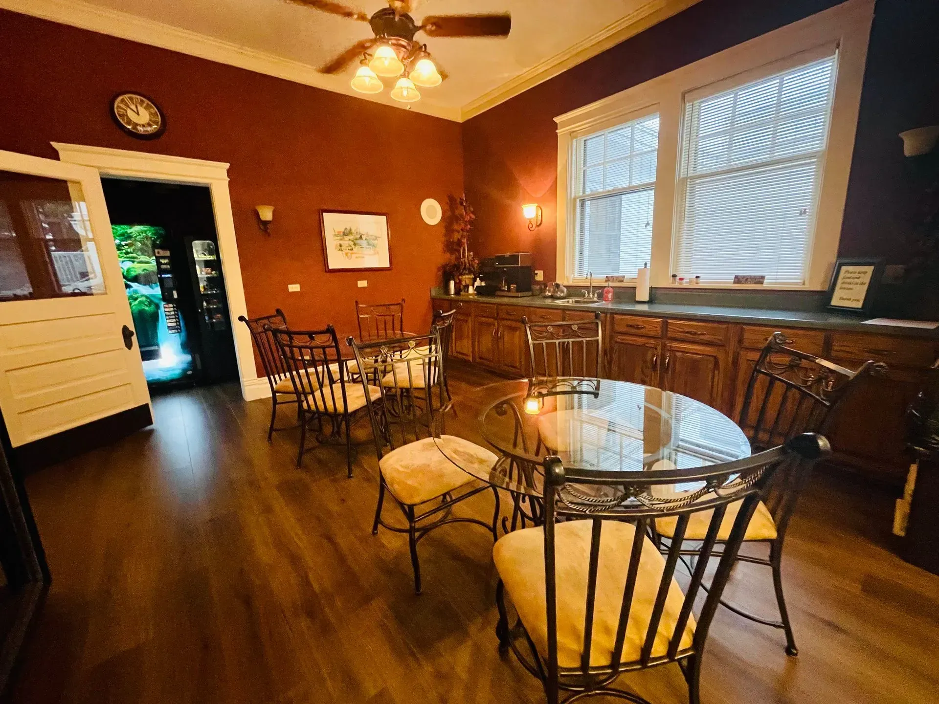 Warm dining room with wooden floors, round table, metal chairs, and sunlight through a large window