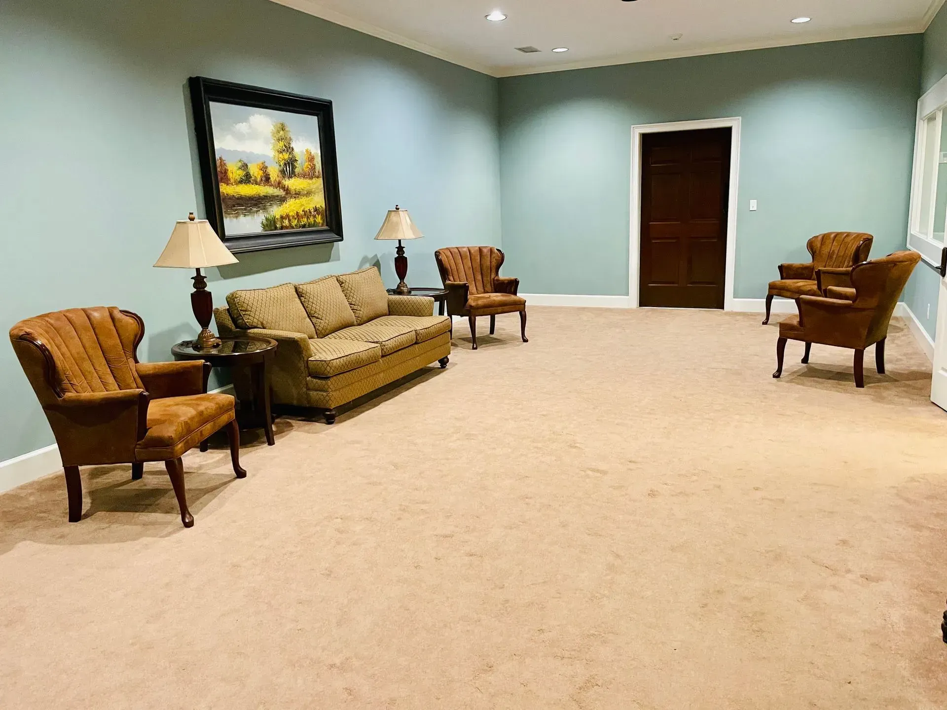 Spacious beige waiting room with green walls, sofa, armchairs, lamps, and a framed painting