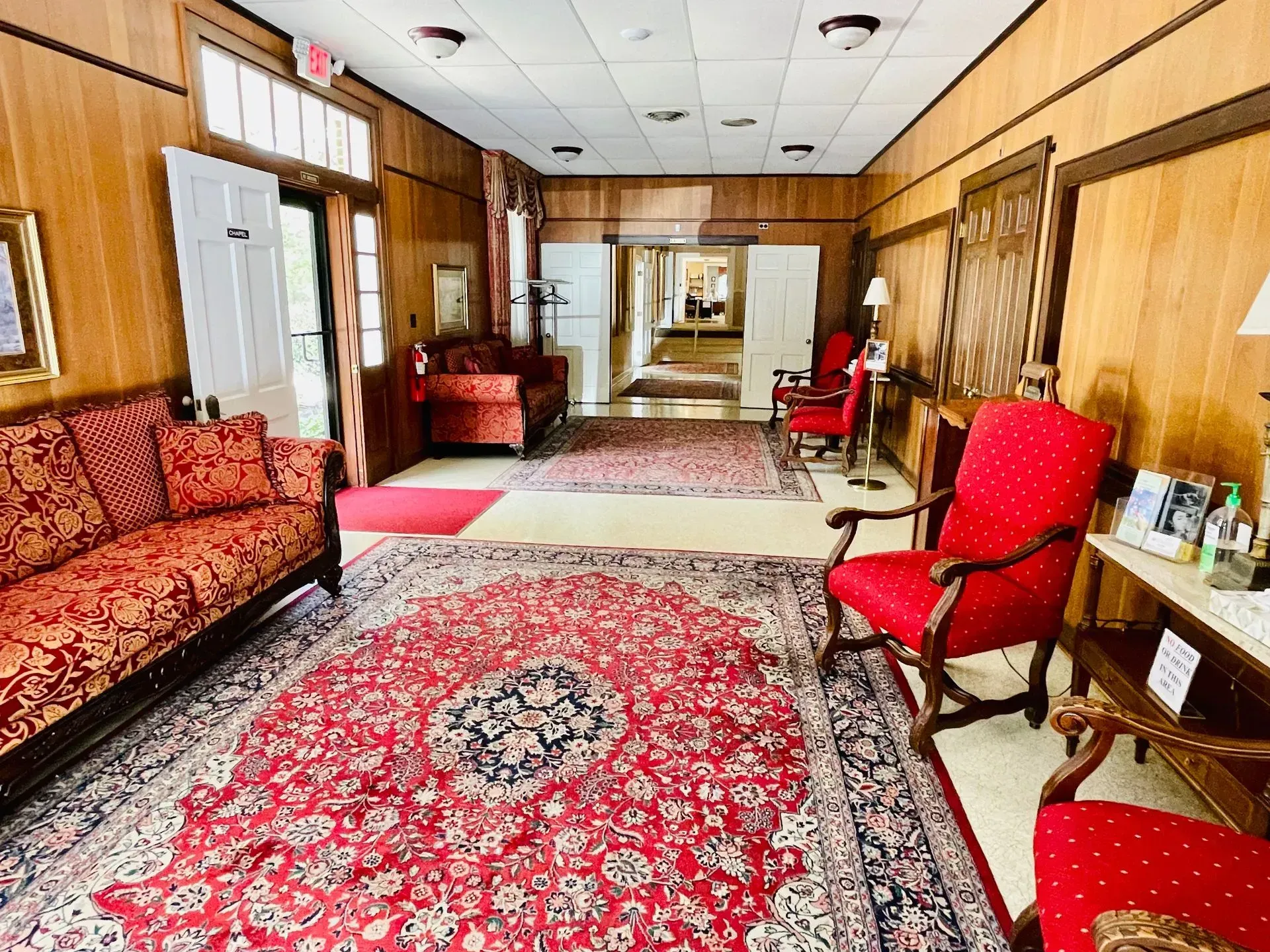 Wood-paneled lobby with red patterned rugs and upholstered chairs in a narrow hallway