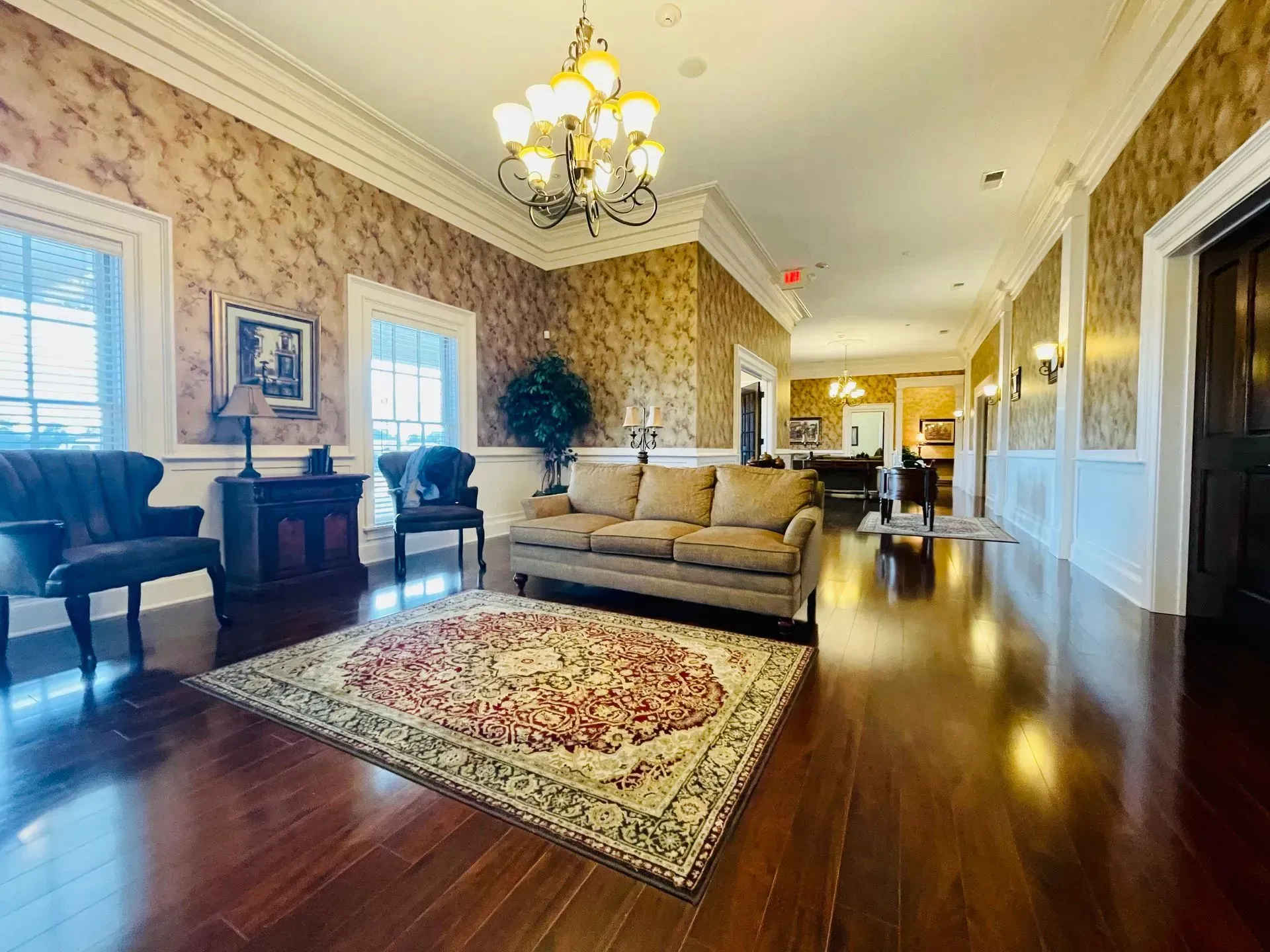 Elegant living room with beige sofa, chandelier, patterned rug, and polished wood floors