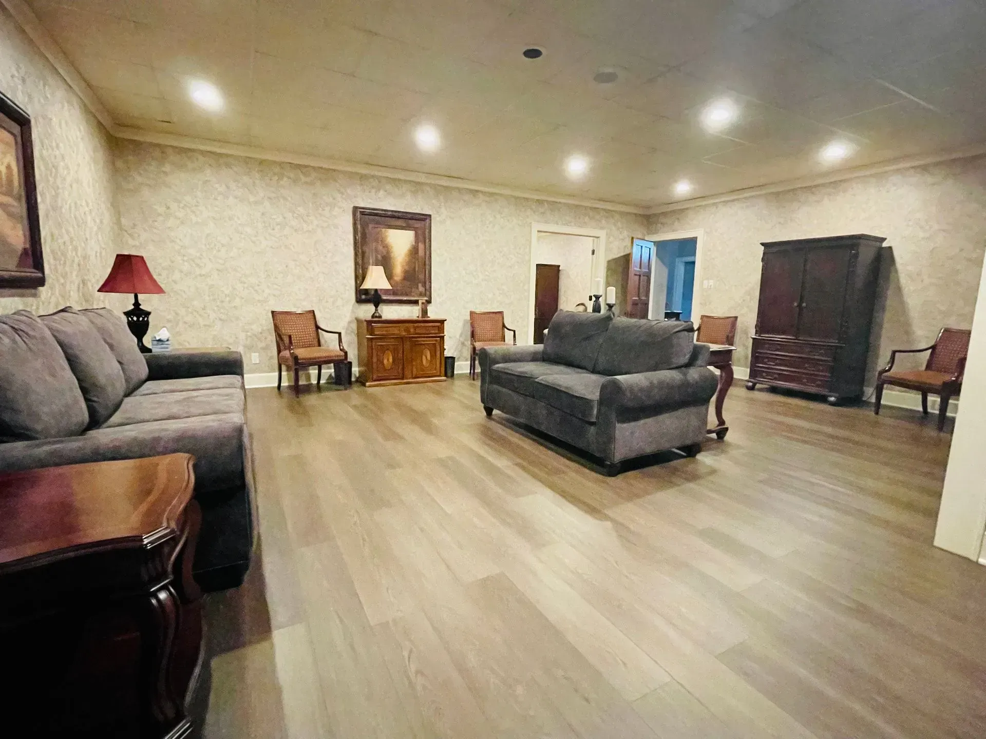 Spacious beige living room with gray sofas, wooden floors, lamps, and a small desk at the far wall