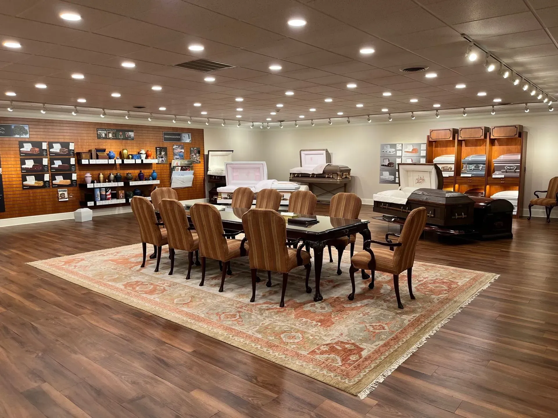 Spacious showroom with a long dining table and chairs on a large patterned rug under recessed ceiling lights.