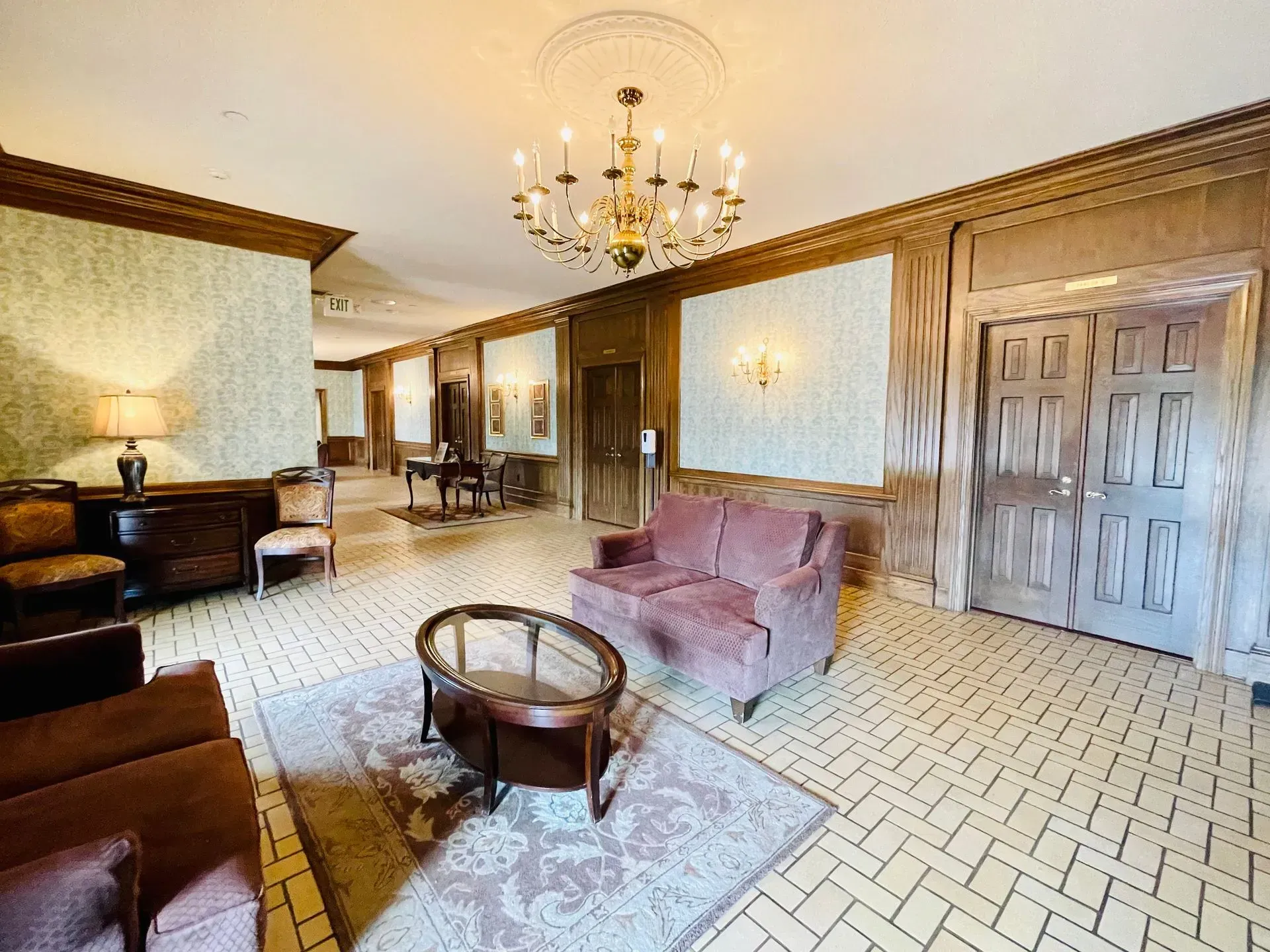 Elegant living room with chandelier, pink sofa, patterned tile floor, and wooden furniture.