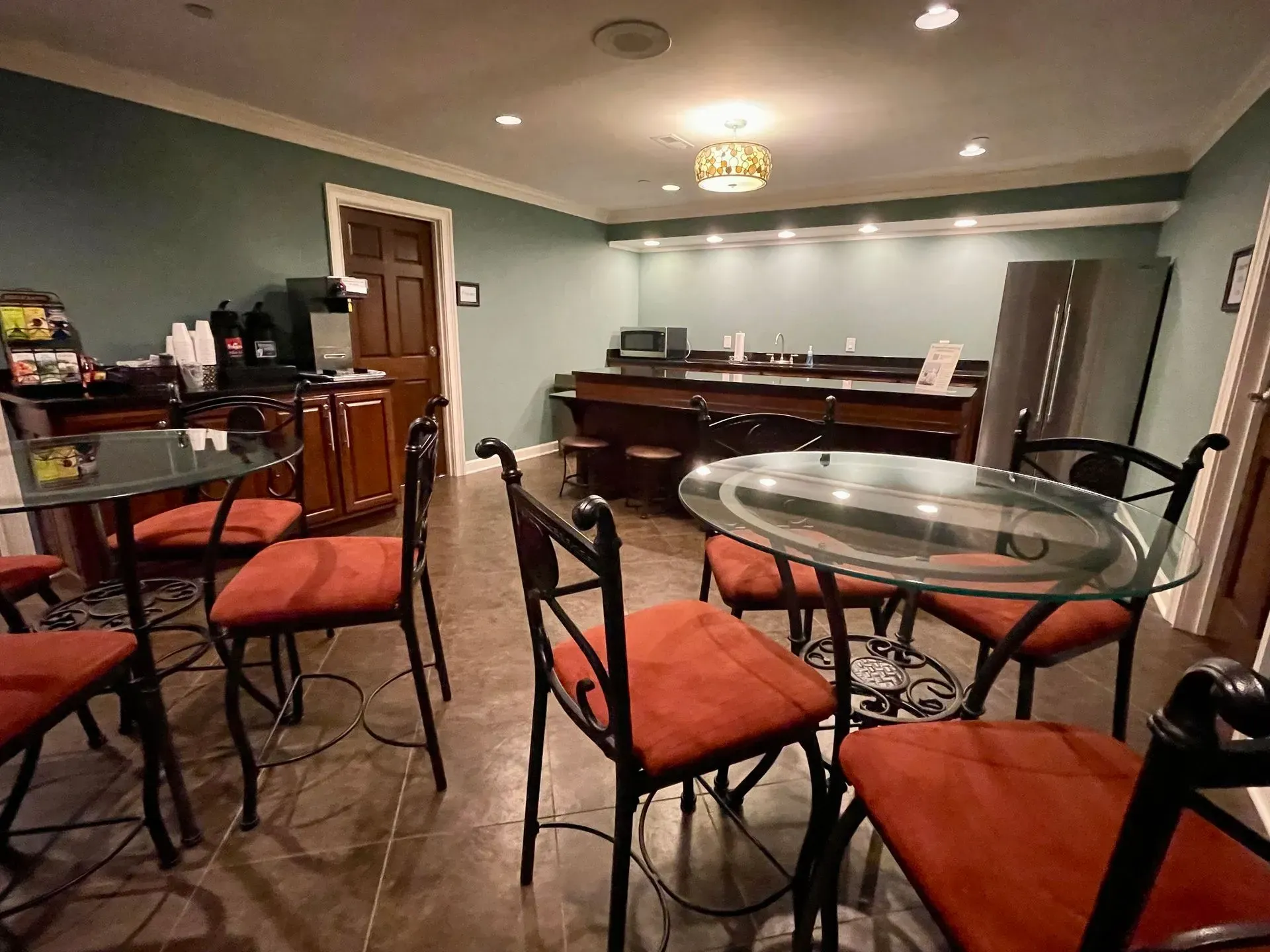 Empty banquet room with red chairs, round glass tables, and a piano against the back wall