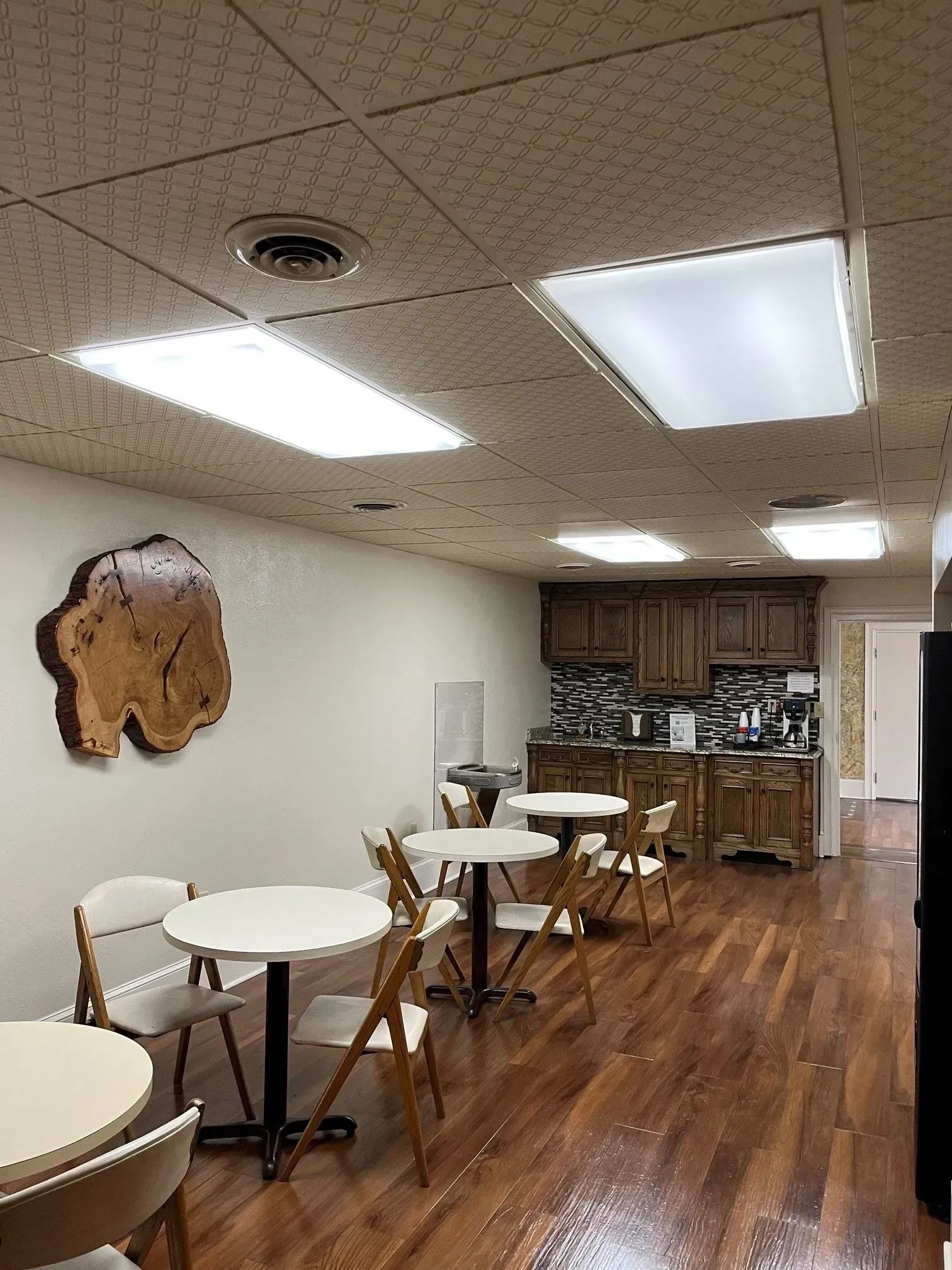 Cozy cafe interior with round tables, chairs, wood flooring, and a small counter at the back.