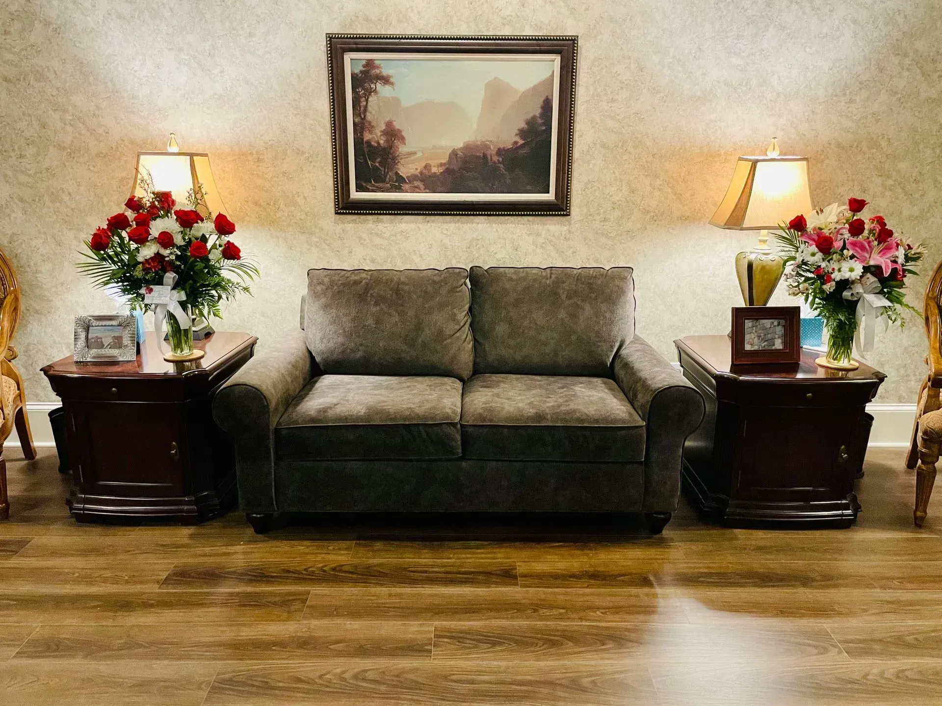 Living room with a gray loveseat, matching side tables, lamps, flowers, and framed wall art