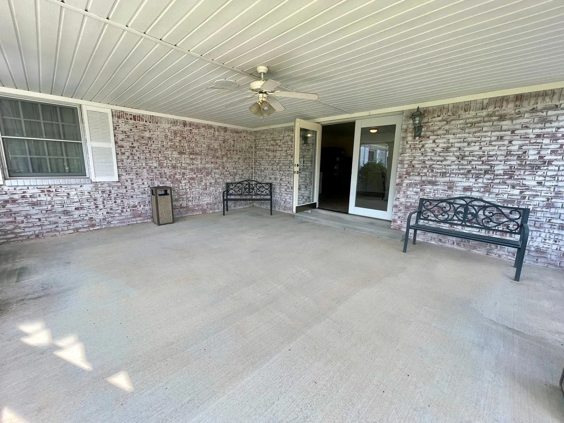 Covered front porch with white brick walls, ceiling fan, benches, and a screened door.