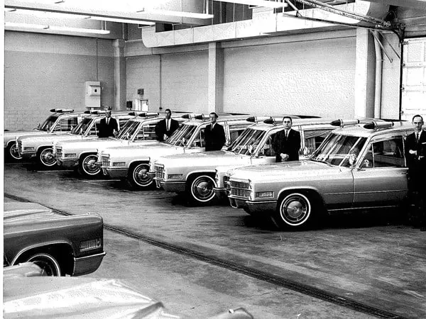 Vintage police cars lined up in a garage, with officers standing beside them.
