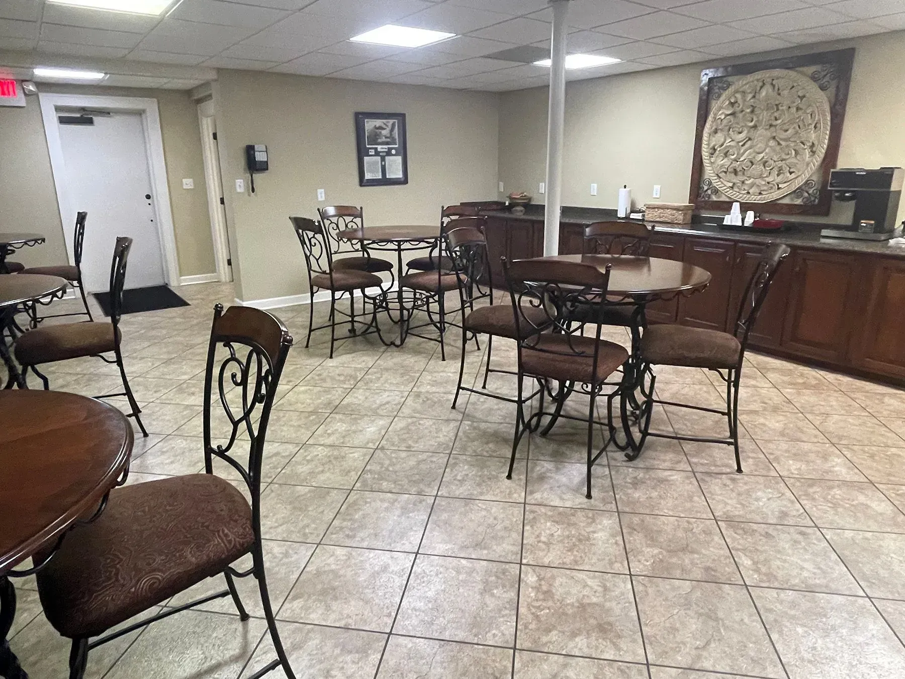 Empty lounge with tables and chairs on a tiled floor, and a large decorative wall panel in back