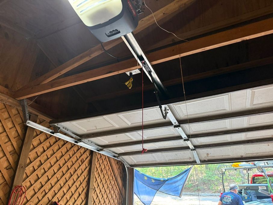 Open garage with raised door, ceiling opener, and parked car visible outside.