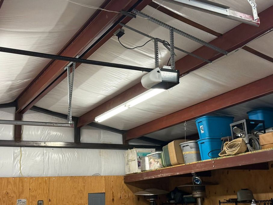 Interior of a warehouse with a red steel roof, white insulation, and a ceiling-mounted projector above stacked storage boxes