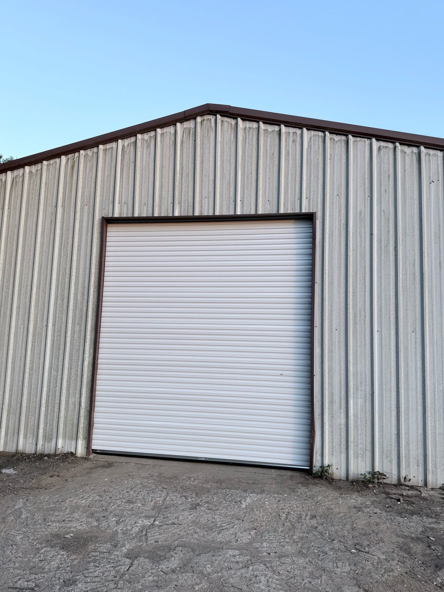 White roll-up door on a gray metal warehouse with gravel in front under a blue sky