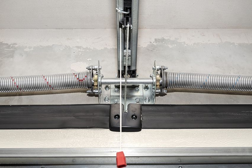 Garage door spring and center bracket on a metal track, with a red safety stop below