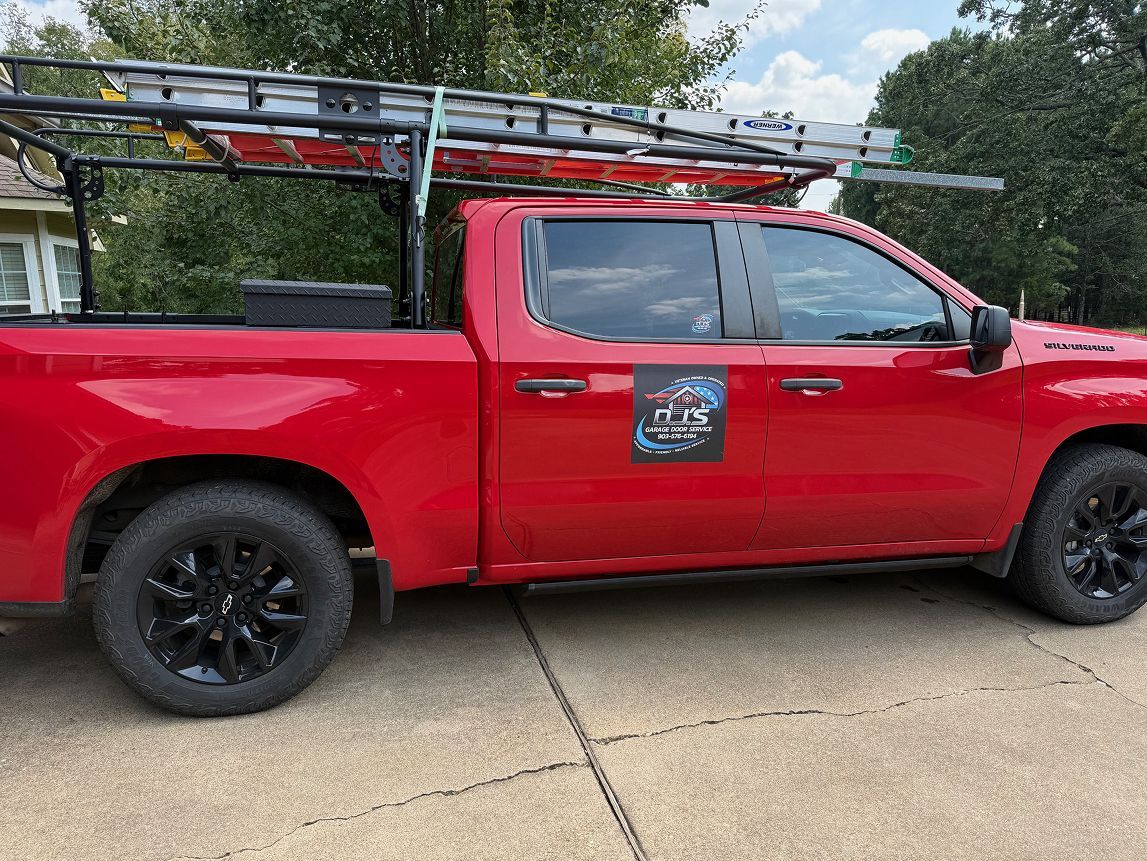 Red pickup truck with ladder racks parked on a concrete driveway outdoors.
