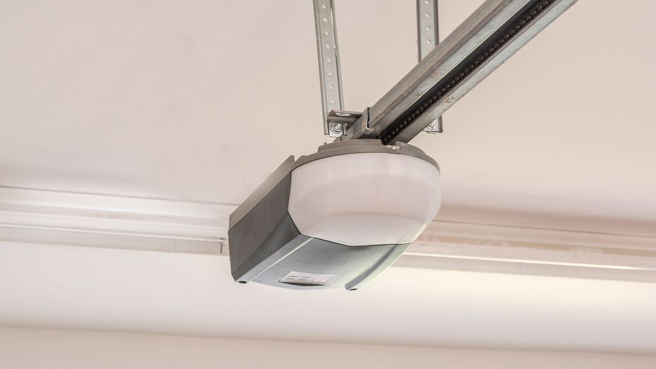 Garage door opener mounted on a ceiling rail with a white light cover.