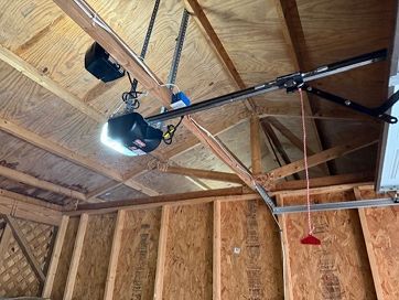 Garage ceiling with open wooden rafters, a work light, and a garage door opener track.