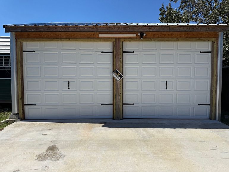 Two white garage doors with a wooden post between them on a concrete driveway under a blue sky