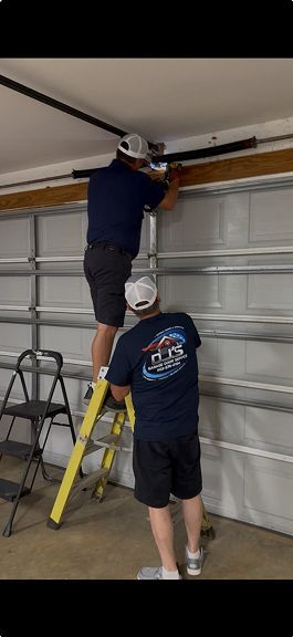 Two workers repairing a garage door opener on a ladder and step stool