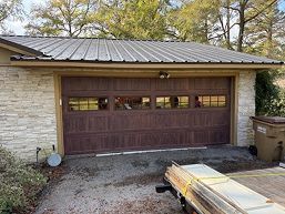 Wood-paneled garage door on a stone house with a metal roof and driveway in front