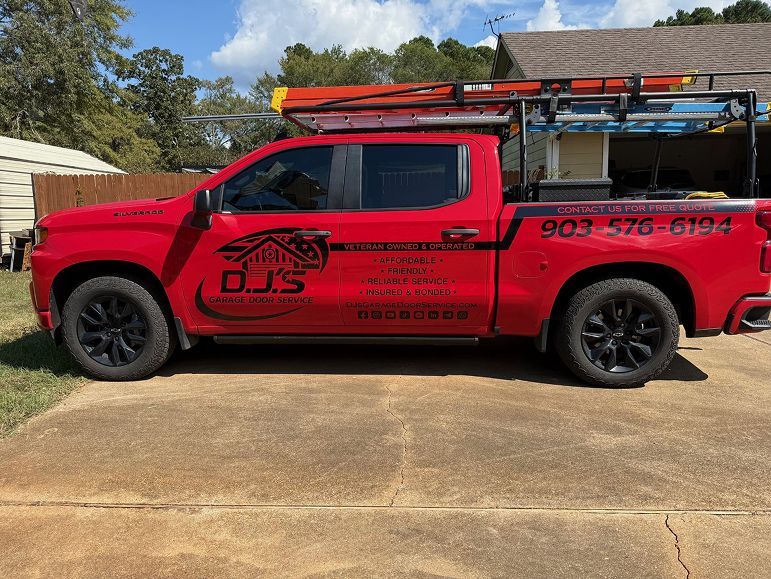 Red pickup truck with company decals and roof racks parked on a concrete driveway outdoors.