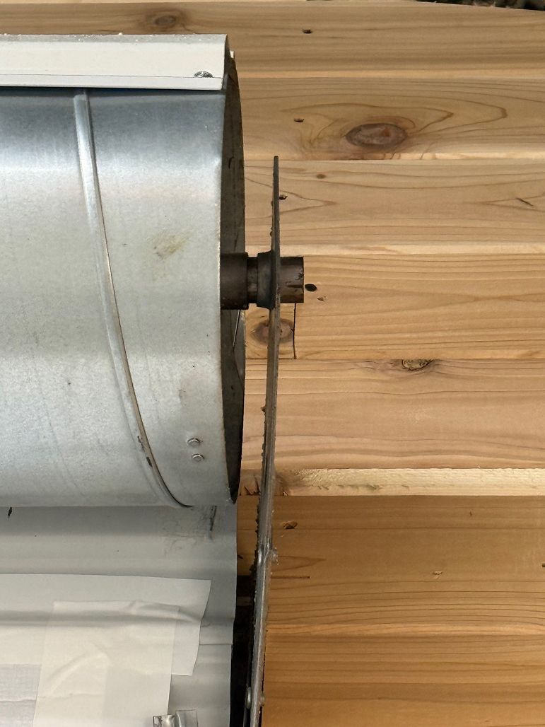 Close-up of a silver metal spool mounted on a wooden surface, with a small bolt and washer protruding.