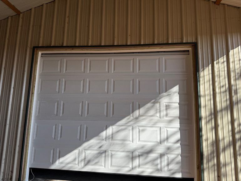 White garage door on a tan wood-sided building, partly covered by a diagonal shadow.