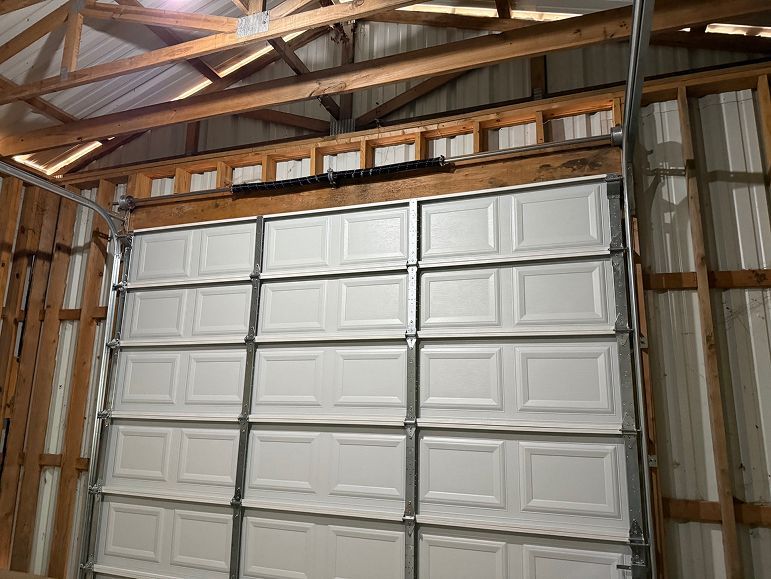 Closed white garage door inside a wooden-framed barn with metal siding and exposed rafters