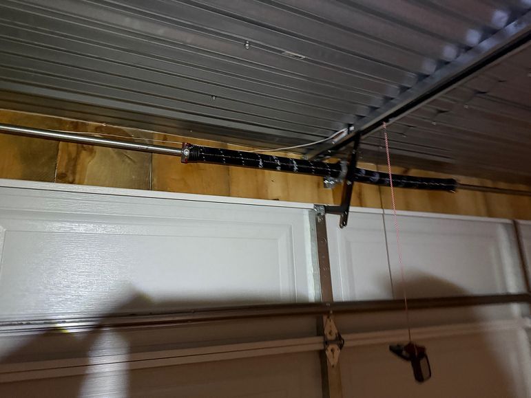 Garage door with a black garage door opener rail mounted under a corrugated metal ceiling.