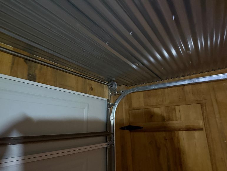 Corrugated metal ceiling above a wooden wall and white cabinet in a small room