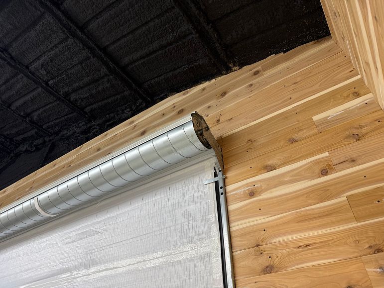 Wooden wall with a white roll-up garage door and black ceiling beams overhead