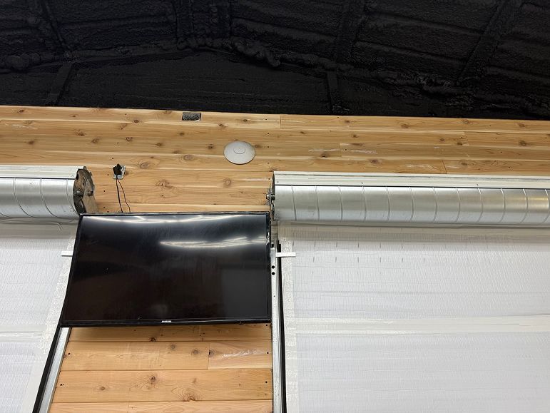 Black metal panel attached near a wooden beam above a white roller shutter.