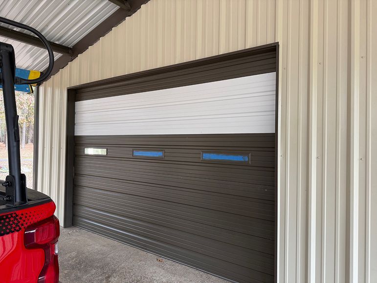 Partially open brown roll-up garage door on a metal building, with a red vehicle at left edge.